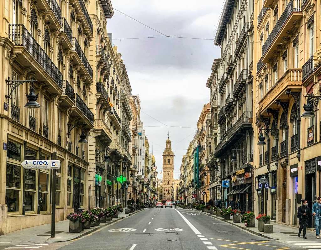 Historic street view in Valencia, Spain with traditional Mediterranean architecture and a church tower in the distance.
